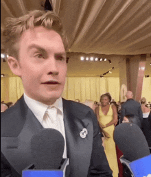 a man in a tuxedo is talking into a microphone at a party