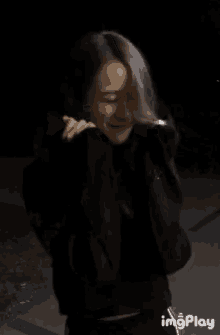 a woman in a black jacket is dancing in the dark with imgplay written in the corner