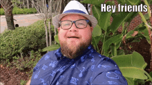 a man with a beard wearing glasses and a hat says " hey friends "