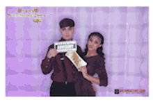 a man and a woman are posing for a picture in a photo booth with a purple background .