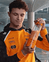 a man in an orange dell sweatshirt is holding a blender filled with orange liquid .