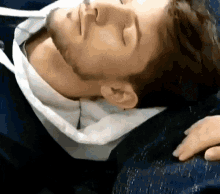 a man is laying down with his eyes closed and a woman 's hand on his shoulder