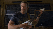 a man playing a guitar in front of a chalkboard that says " wear a cup "