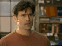 a man in a red shirt is standing in front of a bookshelf with books on it .
