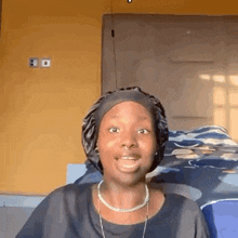 a woman wearing a sleep cap and a necklace is smiling while sitting on a bed .