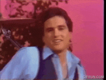 a man in a blue shirt and vest is standing in front of a pink background .