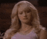a blonde woman in a purple tank top and necklace is looking at the camera .