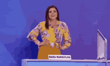 a woman in a yellow floral shirt is standing in front of a sign that says mara maravilhosa