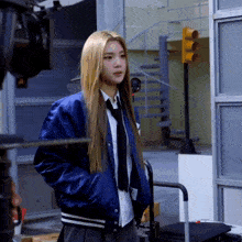 a woman in a blue jacket and tie stands in front of stairs