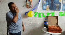a man covering his mouth in front of a wall with feliz written on it