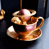 a gold cup and saucer with a pink ball on top of it