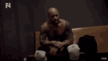 a man without a shirt sits on a bench with boxing gloves on his knees