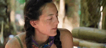a woman with braids and a bandana around her neck is sitting in the jungle .