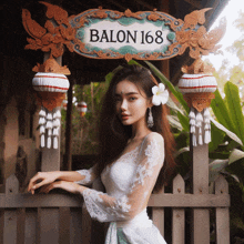 a woman in a white dress stands in front of a sign for balon 168