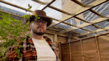 a man wearing a hat and glasses is standing in front of a wooden fence .