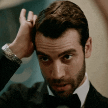 a man in a tuxedo has his hand on his hair