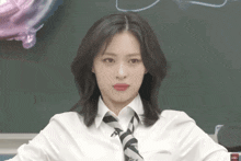 a woman wearing a white shirt and tie is sitting in front of a chalkboard