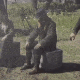 a man with a beard is sitting on a box in a field with a woman sitting next to him .