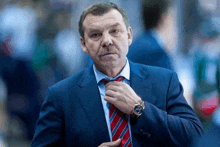 a man in a suit and tie adjusts his tie while wearing a watch