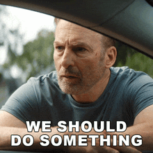 a man sitting in a car with the words we should do something below him