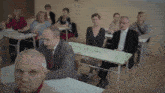 a group of people are sitting at desks in a classroom with a green board that says " a "