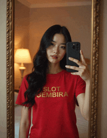 a woman in a red shirt that says slot gembira takes a selfie in a mirror