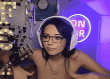 a woman wearing headphones and glasses is standing in front of a neon sign that says on r