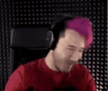 a man with pink hair is sitting in a chair wearing headphones .