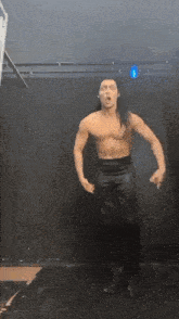a shirtless man with long hair is dancing in a dark room .