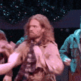 a man with long hair and a beard is wearing a trench coat and a scarf .