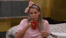 a woman is sitting on a bed holding a cup of coffee and a book .
