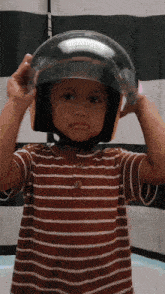 a young boy wearing a striped shirt is putting on a motorcycle helmet
