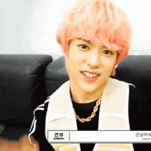 a young man with pink hair is smiling and wearing a black shirt