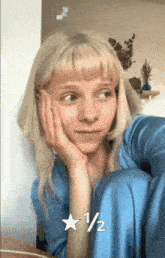a woman with blonde hair is sitting down with her hand on her face and a 1/2 star on the bottom