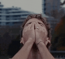 a man is covering his face with his hands while wearing a ring on his finger .
