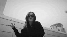 a black and white photo of a woman wearing sunglasses making a peace sign