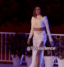 a woman in a white dress is walking on a balcony with a caption that says @tvresidence