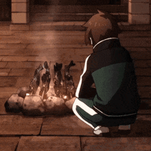 a man in a green and black jacket sits in front of a fire