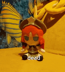 a stuffed doll with red hair is sitting on a yellow couch with the word dead written on it