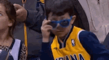 a young boy wearing sunglasses is covering his eyes while sitting in a stadium .