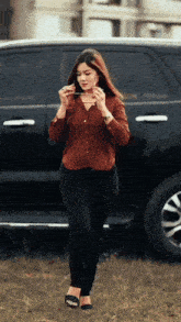 a woman in a brown shirt and black jeans is standing in front of a black suv