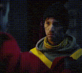 a man wearing a hoodie with yellow stripes on the sleeves looks at the camera