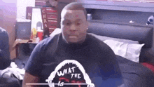 a man wearing a black shirt with a shark on it is sitting on a bed in a room .