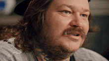 a man with long hair and a beard has a tattoo on his neck that says ' i 'm sorry '
