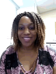 a woman with braids is smiling in front of a wall that has a sign on it that says ' a '