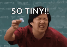 a man is holding a piece of paper in front of a blackboard with the words so tiny written on it .