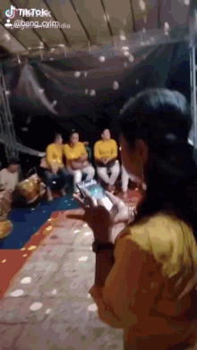 a woman in a yellow shirt is holding a cell phone in front of a group of men in yellow shirts