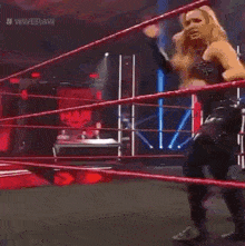 a woman is standing in a wrestling ring with a rope .