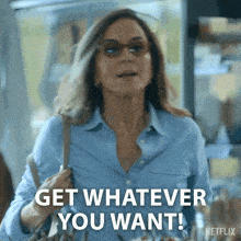 a woman in a blue shirt is holding a purse and saying get whatever you want