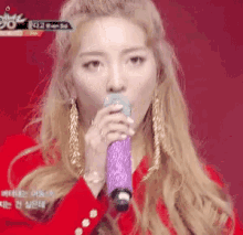 a woman singing into a purple microphone with a red background